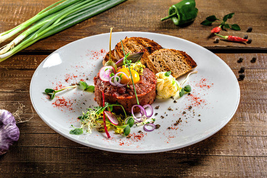 Gourmet tartare, toasted bread and salad on a plate. Delicious healthy French cuisine meal made of raw meat on a rustic wooden table.