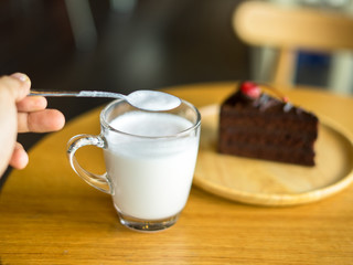 Hand holding glass of milk with chocolate cakes on top red cherry background in wooden plate on wood table