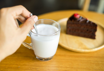 Hand holding glass of milk with chocolate cakes on top red cherry background in wooden plate on wood table