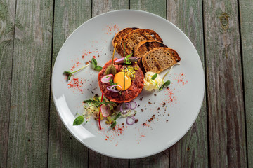Plate with delicious tartare, toasted bread and salad on a wooden table. Healthy gourmet French food made of raw meat. Top view.