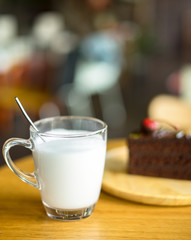 glass of milk with chocolate cakes on top red cherry background in wooden plate on wood table