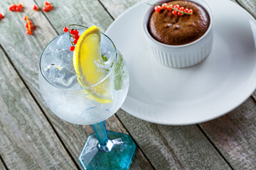 Gin and tonic cocktail with sweet chocolate mousse a wooden table. Alcoholic drinks in a glass with dessert.
