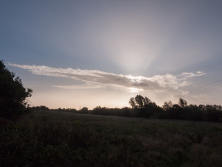 Fototapeta premium beautiful morning rising sun over field with trees through cloud streak