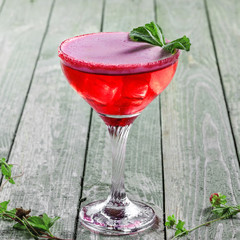 Frozen glass of alcoholic cocktail made of raspberry, mint, martini, vodka and ice. Alcoholic drink on a rustic wooden table.