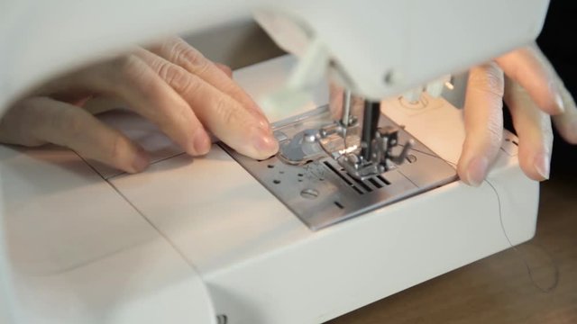 seamstress thread in the needle of sewing machine, sewing machine and woman hands