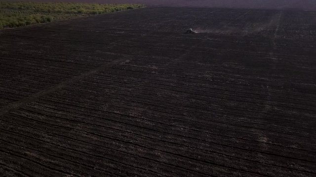 Aerial view of a tractor cultivating a fields with black soil for planting in 4K