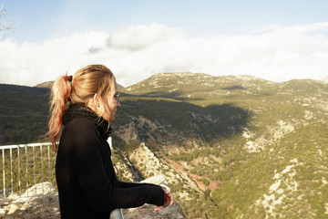 Naklejka premium A middle-aged woman, dyed hair, a sweater and a scarf, stands on a viewing platform in the mountains