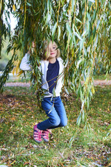 Little child blond girl having fun on a swing outdoor. Girl swinging on a swing made from willow branches. Young child on swing outdoors