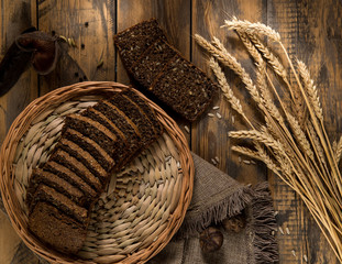 Fototapeta na wymiar Sliced bread in a wicker tray and spikelets on wooden surface