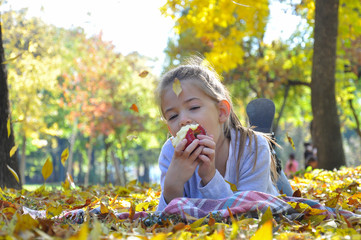 Little girl eats an apple in the park in autumn. Child eating an apple
