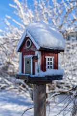 Snötckt fågelbord i form av en stuga