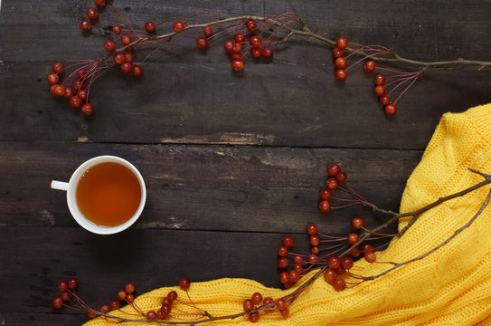 Autumn background boards with dark brown branches with small apples,  Cup of tea and a yellow sweater