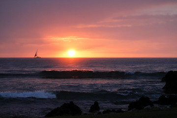 sailboat sailing across setting sun