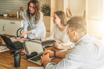 Group of young people working together.Man is using laptop,girls looking on screen of laptop,discussing business plan.Brainstorming, teamwork, startup. Students studying online. E-learning, marketing.