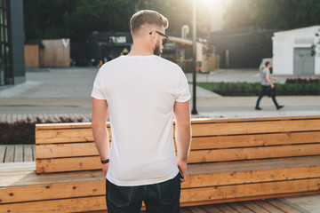Summer day. Back view. Young bearded hipster man dressed in white t-shirt and sunglasses is stands...