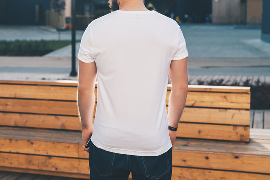 Summer day. Back view. Young bearded hipster man dressed in white t-shirt and sunglasses is stands on city street. Mock up. Space for logo, text, image. Instagram filter, film effect, bokeh effect.