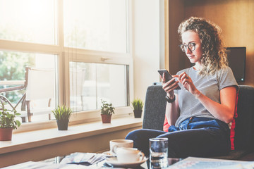 Young businesswoman sits on sofa near window,uses smartphone. Girl chatting, blogging, checking email, working. Student studying. Online marketing,education,e-learning,e-commercesocial medianetwork