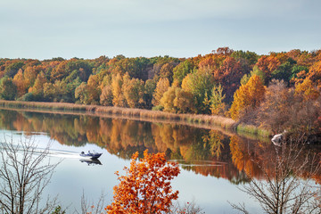 Fall autumn landscape view on the multi colored autumn forest reflecting in the water and boat