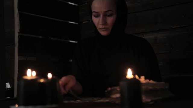 mystical beautiful nun in a black dress, divination on cards with black candlelight