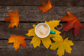 Coffee Cup of cappuccino and autumn leaves on background old dark wood planks.