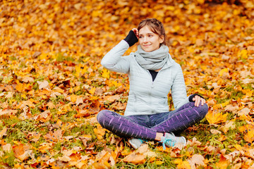 Woman sitting on bright yellow autumnal leaves enjoying beautiful autumn weather in park on forest. Many yellow golden leafs
