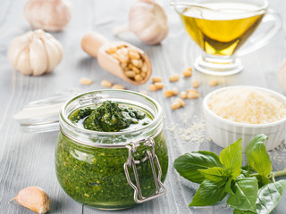 Homemade pesto sauce and ingredients on gray wooden background. Close up wiev of basil pesto in glass jar with ingredients.