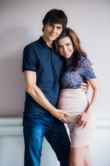 Beautiful pregnant woman and her handsome husband are hugging the tummy, looking at camera and smiling