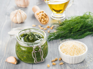 Homemade dill pesto sauce and ingredients on gray wooden background. Close up wiev of dill pesto in glass jar with ingredients.