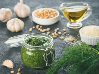 Homemade dill pesto sauce and ingredients on dark cement background. Close up wiev of dill pesto in glass jar with ingredients. Toned image