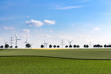 Fototapeta na wymiar Windkrafträder entlang einer Stromtrasse mitten im Feld, Freiraum oben und unten