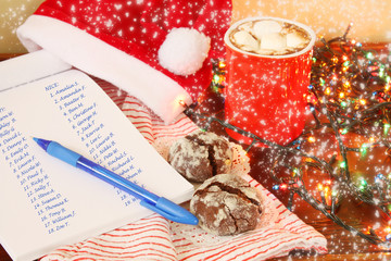 Santa's preparation for christmas presents delivery: winter hot spicy drink cacao with marshmallows and list of names naughty and nice children on background of striped blanket and electric lights