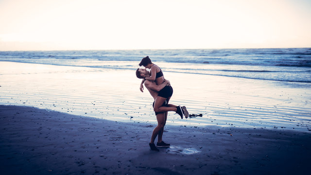Young adult couple kissing on beach after run on beach