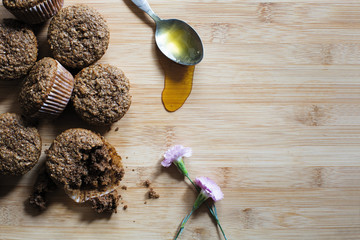 Bran muffins on a wooden surface with honey and purple flowers for decoration