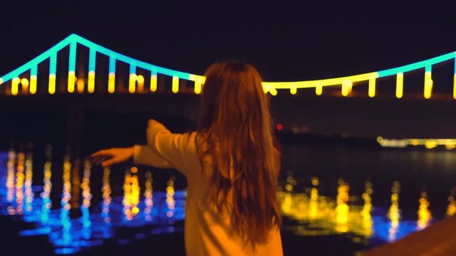a young and sensual woman, an Asian woman with long hair, dances in the night bustle against the backdrop of a glowing fanfare. A sportive style of clothing. bright night illumination and a luminous