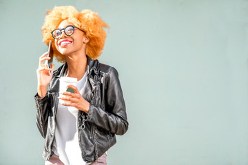 Lifestyle portrait of an african smiling woman in leather jacket talking phone on the green wall background