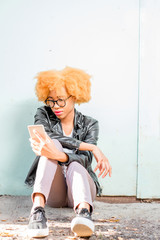 Lifestyle portrait of an african woman in leather jacket sitting with phone on the green wall background