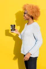 Portrait of a beautiful african woman in blue sweater standing with coffee cup on the yellow background