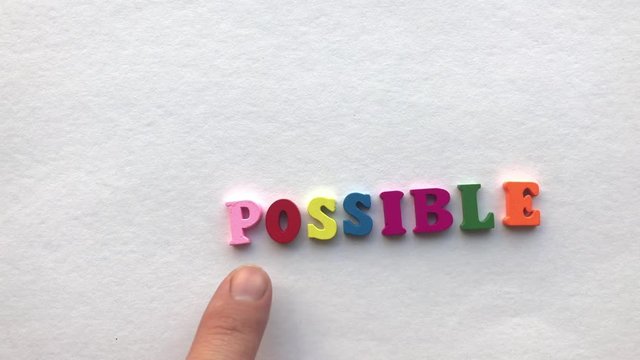 impossible. coloured wooden letters on a white sheet of paper.