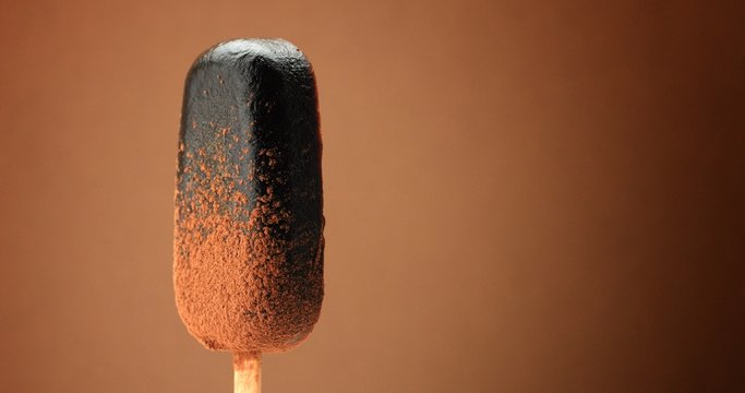 chocolate ice cream on a stick and liquid chocolate covered it. Different chocolate textures. on brown background