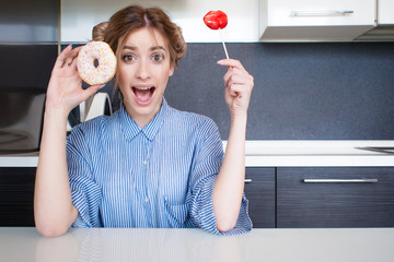 Beautiful young girl with a donut and a Lollipop in the kitchen. To do funny faces