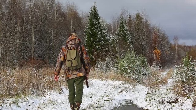 Hunter with hunting rifle and backpack walks through the winter forest