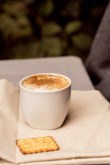 White cup of cappuccino and cracker on napkin