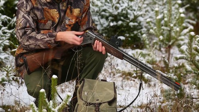 Hunter charges a hunting rifle with cartridges in winter forest