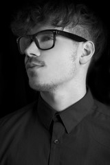 Fashion dark  portrait of sexy young man with glasses on black background. Portrait of intelligent man. Black and white portrait of curly fashion model with glasses on dark  background. Vintrage shot.
