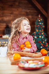 Fototapeta na wymiar Happy little child, cute baby girl at table in home kitchen holds a lot of the orange and have fun in a Christmas interior with tree