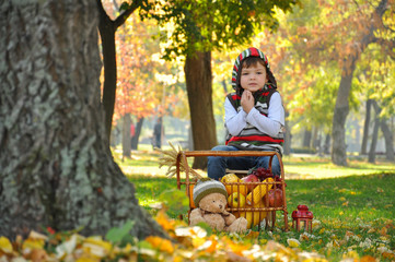 Little boy in the park in autumn with apples and pumpkins. Child play in park in autumn