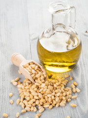 Pine nut oil and pine nuts in wooden scoop on gray wooden background