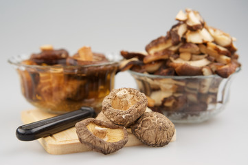 Dry Shitake mushroom or lentnus edodes and knife place on chopping board have blur mushroom soak and cutting piece of mushroom in glass cup