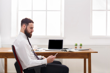 Pensive  businessman in office using cell phone by the laptop