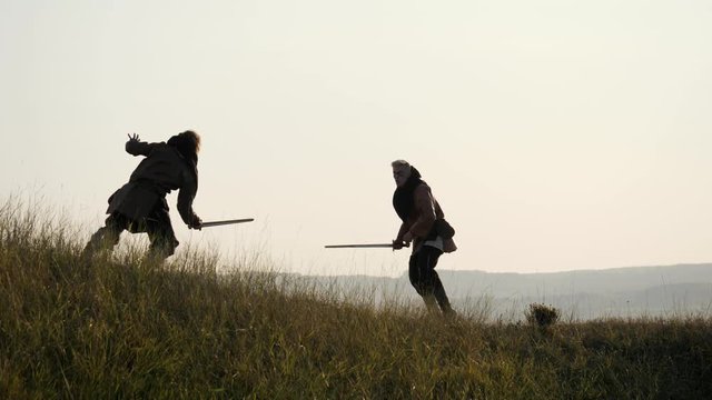 Silhouettes of two warriors Viking are fighting with swords. Contre-jour